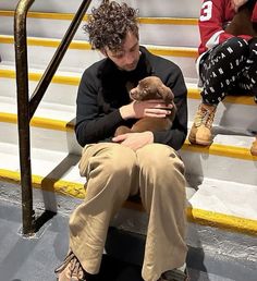 a man sitting on the steps holding a teddy bear in his hands and looking down