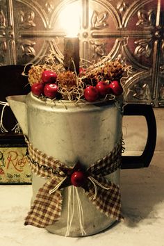 an old tin can has cherries and pine cones in it, tied with twine