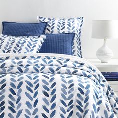 a bed with blue and white comforters on top of it next to a night stand