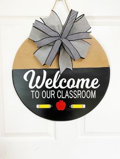 a welcome to our classroom sign hanging on the front door with a bow and an apple