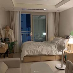 a bedroom with a bed, desk and fan in it's corner area next to a window