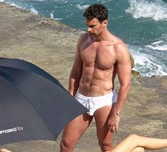 a shirtless man holding an umbrella while standing next to a woman on the beach