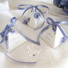 three small white boxes with blue flowers on them and ribbons tied around the top one