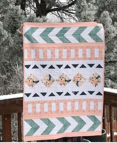 a quilted blanket hanging on the side of a wooden fence in front of snow covered trees