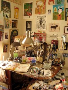 a cluttered desk with lots of art on the wall and pictures all around it