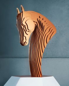 a wooden horse head on top of a white pedestal in front of a gray wall