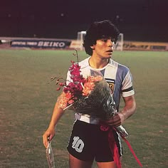 a young man holding a bouquet of flowers on top of a lush green soccer field