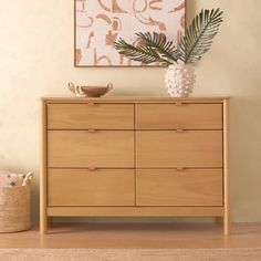 a wooden dresser sitting in front of a painting on the wall next to a basket