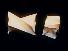 two white origami boats sitting side by side on a black surface in the dark