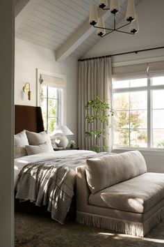 a large bed sitting under a window next to a tall plant in a living room