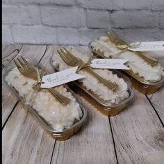 four small containers with forks in them sitting on a wooden table next to a brick wall