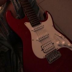 a red guitar sitting on top of a person's lap next to a wall