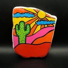 a painted rock with a cactus in the desert on it's side and sun above