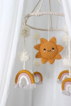 a crocheted sun and rainbow mobile hanging from a white curtain