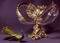 a gold and crystal bird figurine sitting next to a glass bowl with a peacock on it