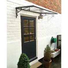 a white brick house with black door and window on the outside, surrounded by potted plants