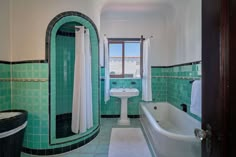 a bathroom with green tiles and a white bathtub next to a sink under a window