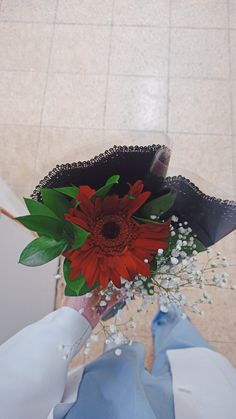 a red flower in a black hat with baby's breath on the floor next to it