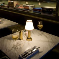 two glasses of wine on a table with silverware and books in the back ground