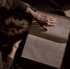 a man sitting at a table with an open book in front of him and his hand on top of it