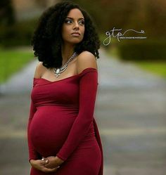 a pregnant woman in a red dress poses for a photo with her hands on her belly