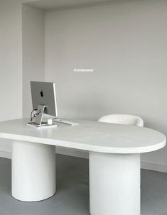 a white table with a computer on it in an empty room next to a chair