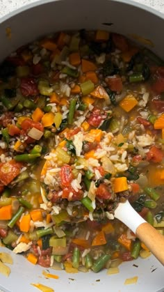 a pot filled with vegetables and rice on top of a counter next to a wooden spoon