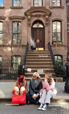 three people sitting on the curb in front of a building