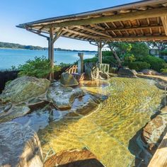 an outdoor hot tub with rocks and water running through it, next to the ocean