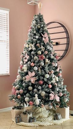 a decorated christmas tree with pink and white ornaments in a living room next to a round clock