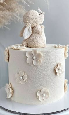 a white cake decorated with flowers and a teddy bear on top is sitting on a table