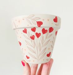 a woman's hand holding up a cup with hearts painted on the outside and inside