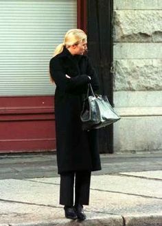 a woman is standing on the sidewalk with her hand in her pocket and looking at something