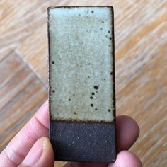 a person holding up a small piece of brown and white tile on a wooden floor