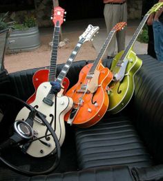 four guitars are lined up in the back of a pickup truck with people standing around