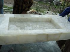 a marble sink sitting on top of a table next to a man standing over it