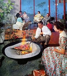 a group of people sitting around a fire pit in a room with large glass windows