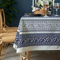 a dining room table covered with a blue and white tablecloth next to two chairs