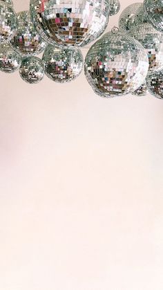 several disco balls hanging from the ceiling in front of a white wall with a pink background