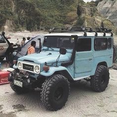 a light blue jeep parked on top of a beach next to a group of people