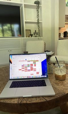 a laptop computer sitting on top of a wooden table next to a jar of liquid