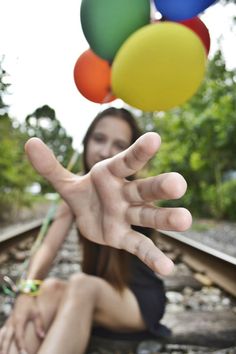 a woman sitting on the train tracks with her hands in the air and balloons floating above her