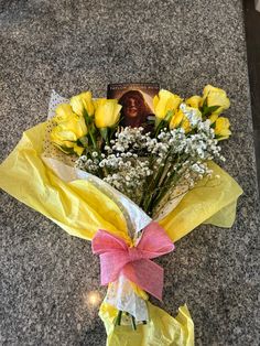 a bouquet of yellow roses and baby's breath wrapped in paper with a pink ribbon