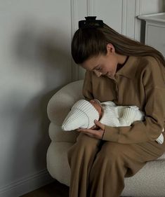 a woman sitting on a chair holding a baby in her lap and looking down at the floor