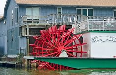 a large red and white water wheel in front of a blue house on the water