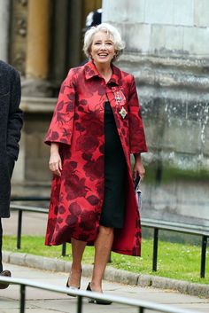 an older woman in a red coat and black dress is walking down the street with her hand on her hip