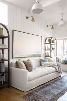 a living room with white couches and wooden floors, along with hanging lamps on the wall