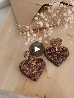 two heart shaped earrings sitting on top of a wooden table next to a vase with flowers