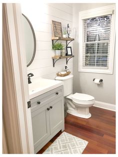 a white toilet sitting next to a sink in a bathroom under a window with wooden floors