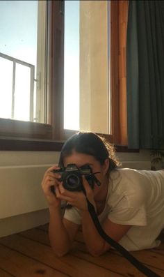 a woman laying on the floor with a camera in front of her and looking through it